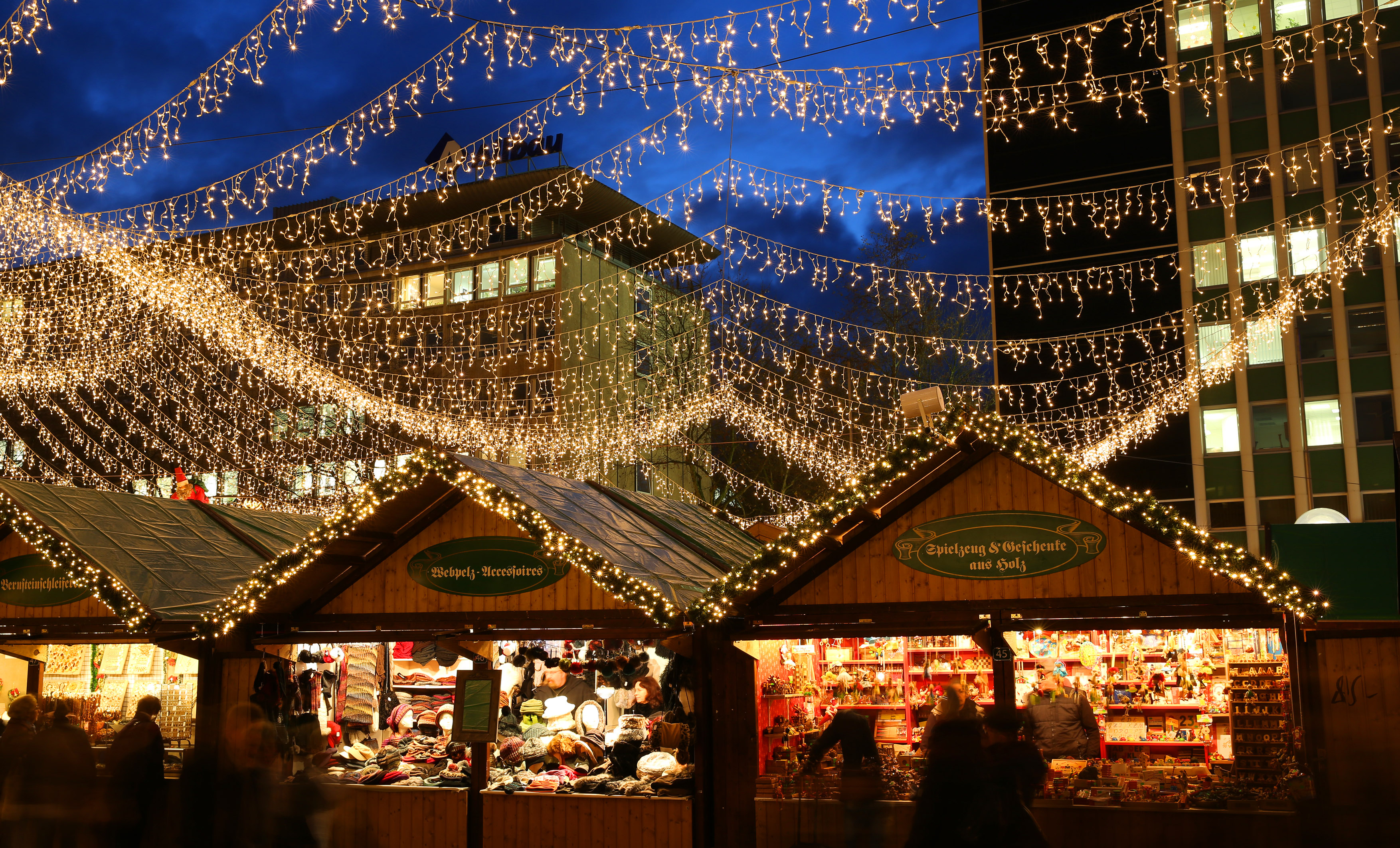 Abendliche Szene eines stimmungsvoll beleuchteten Weihnachtsmarktes mit Besuchenden, Lichterketten und zentral